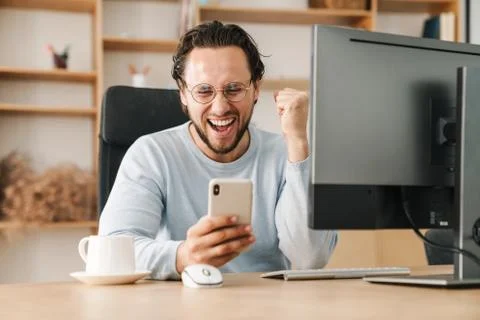 Image of programmer man making winner gesture and using cellphone Stock-Fotos