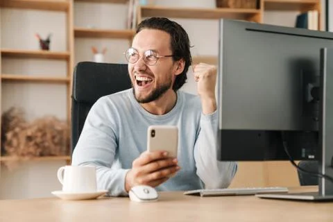 Image of programmer man making winner gesture and using cellphone Stock Photos