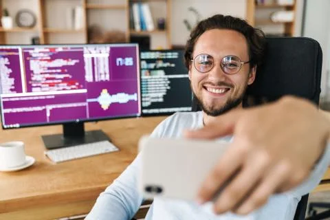 Image of programmer man smiling while taking selfie photo on cellphone Stock Photos