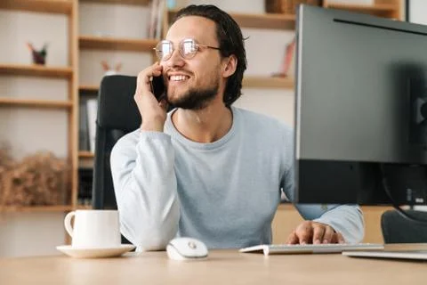 Image of programmer man talking on cellphone while working with computer Stock Photos