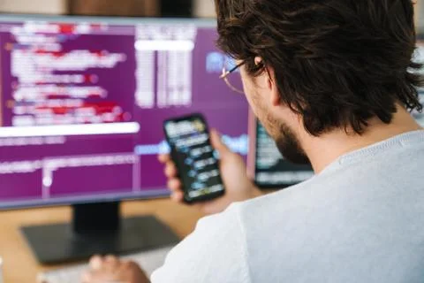 Image of programmer man using smartphone while working with computers Stock Photos