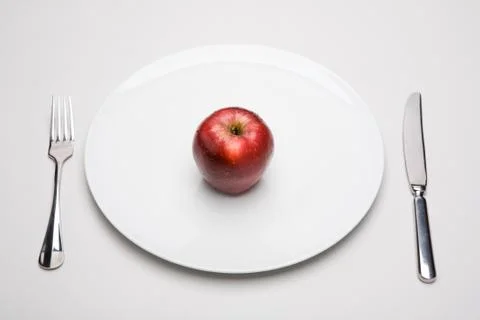 Image of red apple on white plate with fork and knife near by Stock Photos