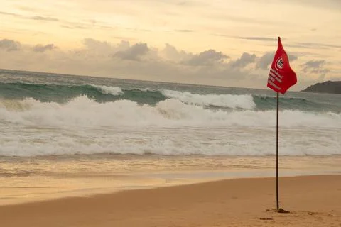 The image of a red flag waving on a sandy beach against a background of dar.. Fotos de archivo