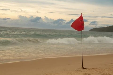 The image of a red flag waving on a sandy beach against a background of dar.. Fotos de archivo
