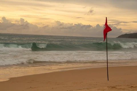 The image of a red flag waving on a sandy beach against a background of dar.. Stock Photos