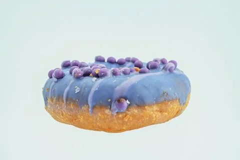 Image shows a floating, single blue iced doughnut with decorative purple spec Stock Photos