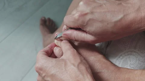 The image shows a man using precision to trim his toenails with a pair of metal Stock Footage 346410766