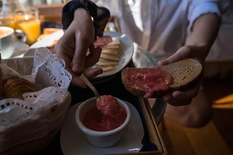 The image shows a person preparing breakfast by spreading jam on a slice of b Stock Photos
