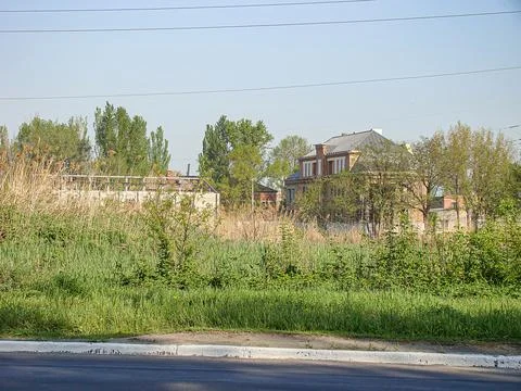 The image shows a run-down, vacant brick house amidst lush overgrowth in a su Stock Photos