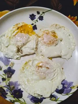 The image shows three fried eggs on a plate, with the yolks still runny. Stock Photos