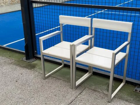 This image shows two white plastic chairs on a sunny concrete surface, next.. Stock Photos