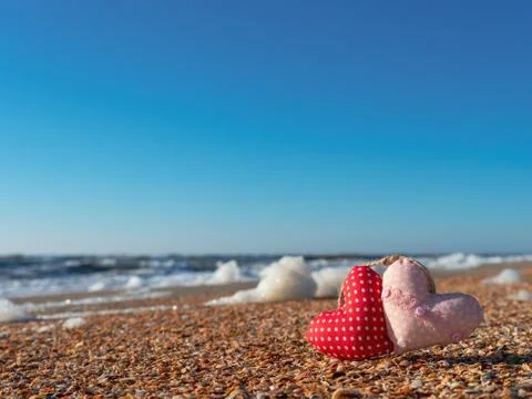Image of a soft toy in the shape of a heart on the beach. Stock Photos