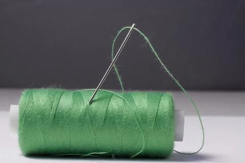 Image of a spool with a green thread and a needle. Stock Photos