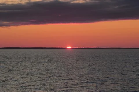 Image of the sun setting in the sea behind the island Stock Photos