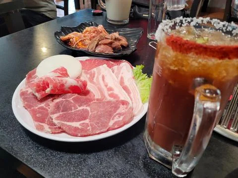 Image of a table with various cuts of raw meat and a glass of michelada Stock Photos