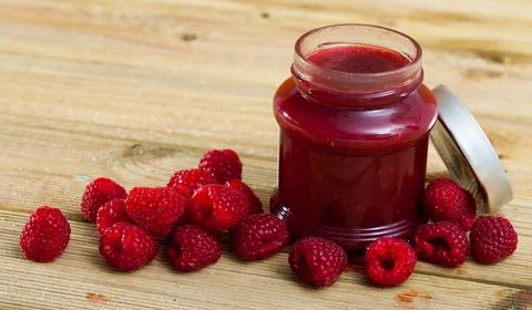 Image of tasty raspberry jam in jar and fresh berries on wooden surface Stock Photos