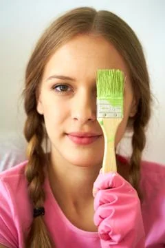 Image of teenage girl hiding one of her eyes behind paintbrush with green color Stock Photos