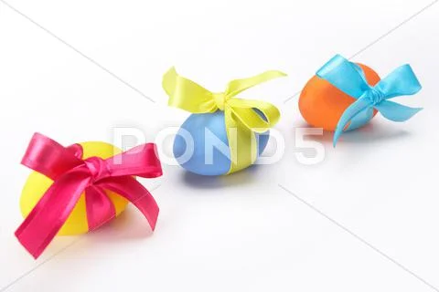 Image of three multicolored eggs tied by silk ribbons on white background Stock Photos