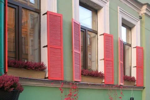Image of three windows with red shutters and flowers on the windowsills Stock Photos