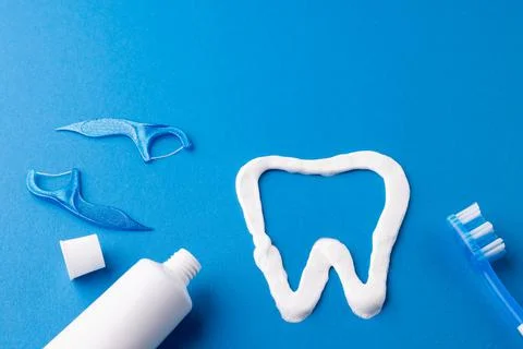 Image of toothbrush, toothpaste, strings and tooth made of paste on blue surface Foto stock