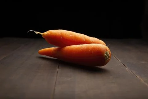 Image of two carrots close up on rustic wooden surface and black background Foto stock