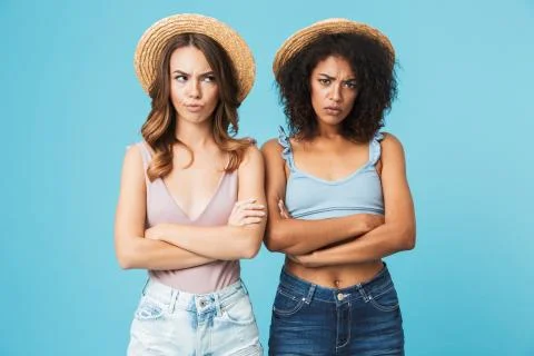 Image of two negative women with different color of skin in straw hats and sw Stock Photos