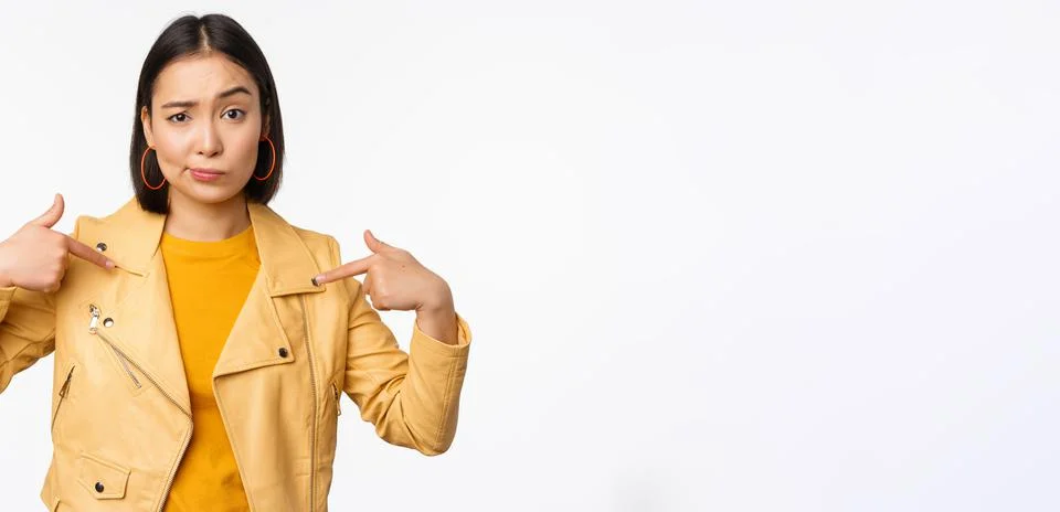 Image of unamused asian girl pointing at herself, looking with disbelief Stock Photos