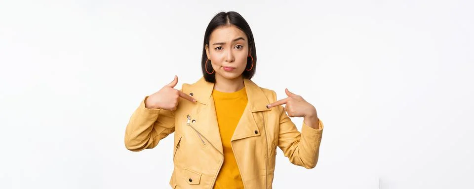 Image of unamused asian girl pointing at herself, looking with disbelief Stock Photos