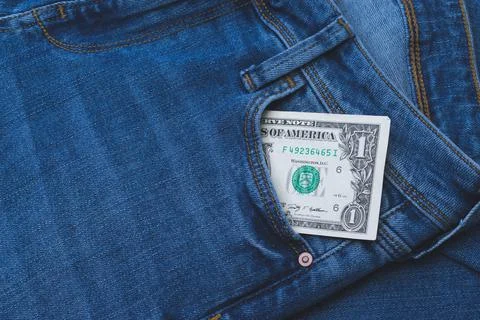 An image of a US one dollar banknote sticking out of a pocket of blue jeans. Stock Photos