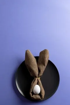 Image of white easter egg and bunny ears on black plate and copy space on purple 스톡 사진