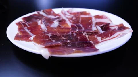 Image of a white plate with serrano ham on a black background Stock Photos