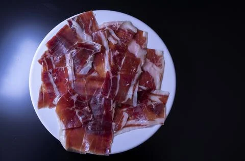 Image of a white plate with serrano ham on a black background Stock Photos