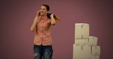 Image of woman talking on smartphone with stack of boxes on red background Stock Photos