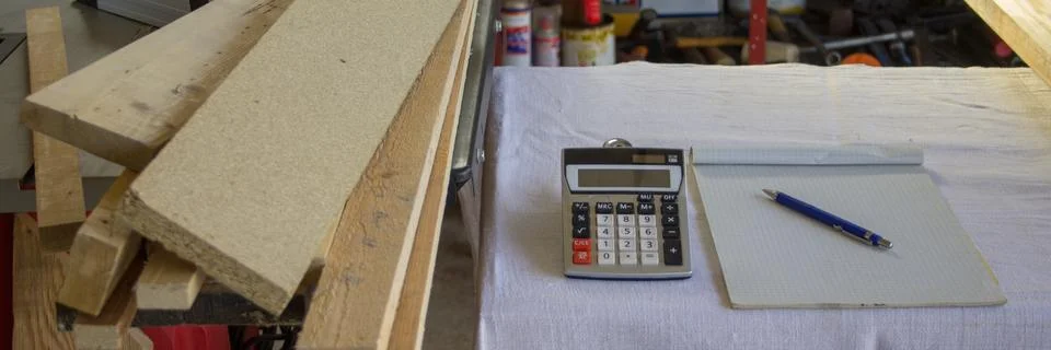 Image of a workbench in a workshop with a calculator, notepad, and wooden boards Stock Photos