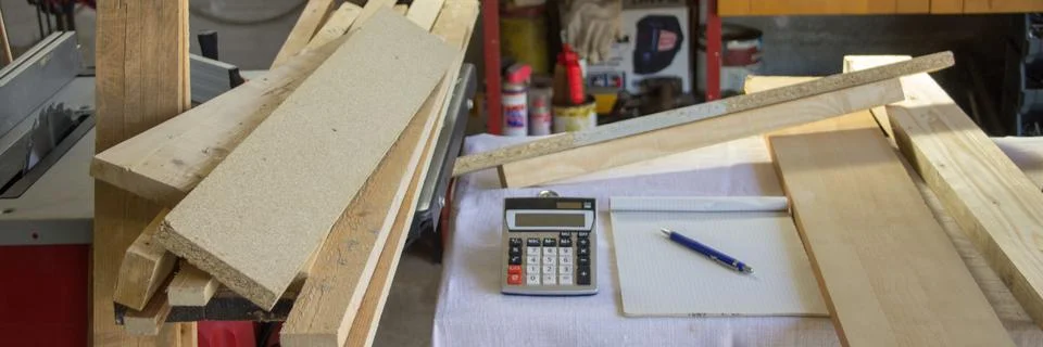 Image of a workbench in a workshop with a calculator, notepad, and wooden boards Foto stock