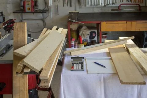 Image of a workbench in a workshop with a calculator, notepad, and wooden boards Stock Photos