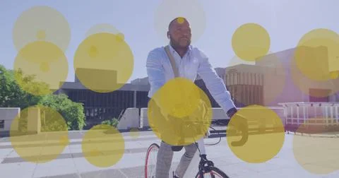 Image of yellow dots over african american businessman riding on bike in city Ilustração Stock