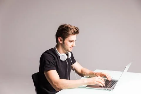 Image of a young man at computer desk working on laptop with headphones on wh Stock Photos