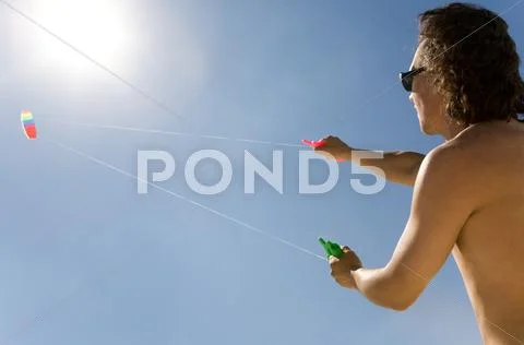 Image of young man flying a colorful kite into bright blue sky with shining sun Stock Photos
