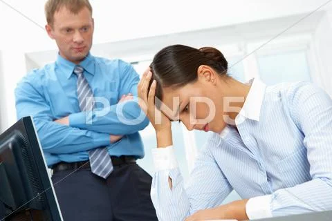Image of a young upset businesswoman, her chief standing at her distressed Stock Photos