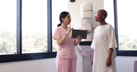 Imaging tech using tablet, explaining mammogram prep to African American patient Stock Footage 334841933