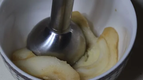 Immersion blender transforming cooked fruit slices into smooth puree inside Stock Footage 329621638