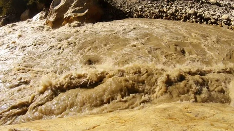 Impetuous spring brown stream of water from melted snow with mud sun reflects ro Stock Footage 106109515