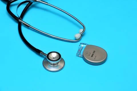 An implantable pacemaker device and a stethoscope on a blue background. Stock Photos