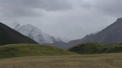 Imponent snowy mountain with clouds and yellow greenish field in foreground, 4K, Video stock 150120629
