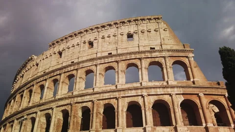 Imposing arches of the Colosseum with a cloudy sky are painted orange at sunset Stock Footage 137133376