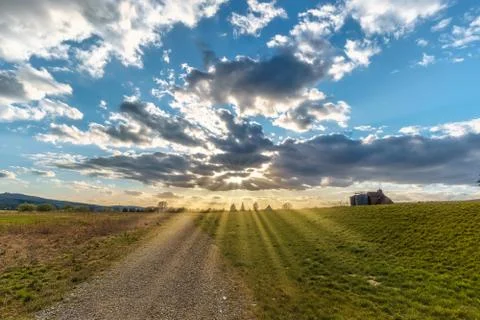 An imposing cloud sky in a landscape of fields and a path where sun rays come Foto stock