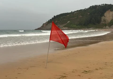 An imposing red flag flutters in the wind on a sandy beach, warning of danger Stock Photos