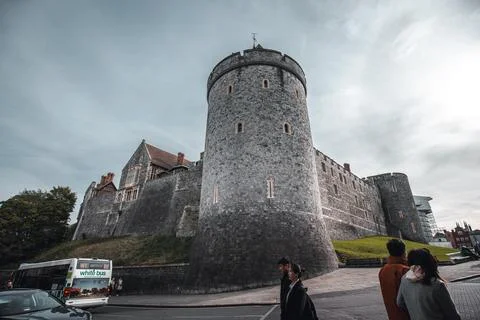 An imposing stone castle with a round tower stands against a cloudy sky, a bus Stock Photos