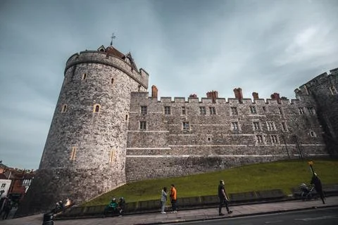 An imposing stone castle wall with a tower on the left, a grassy hill, and Stock Photos